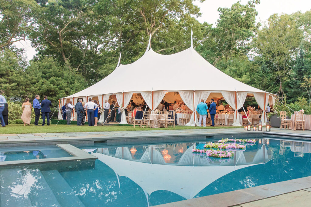 Outdoor wedding tent venue with guests mingling beside the swimming pool.