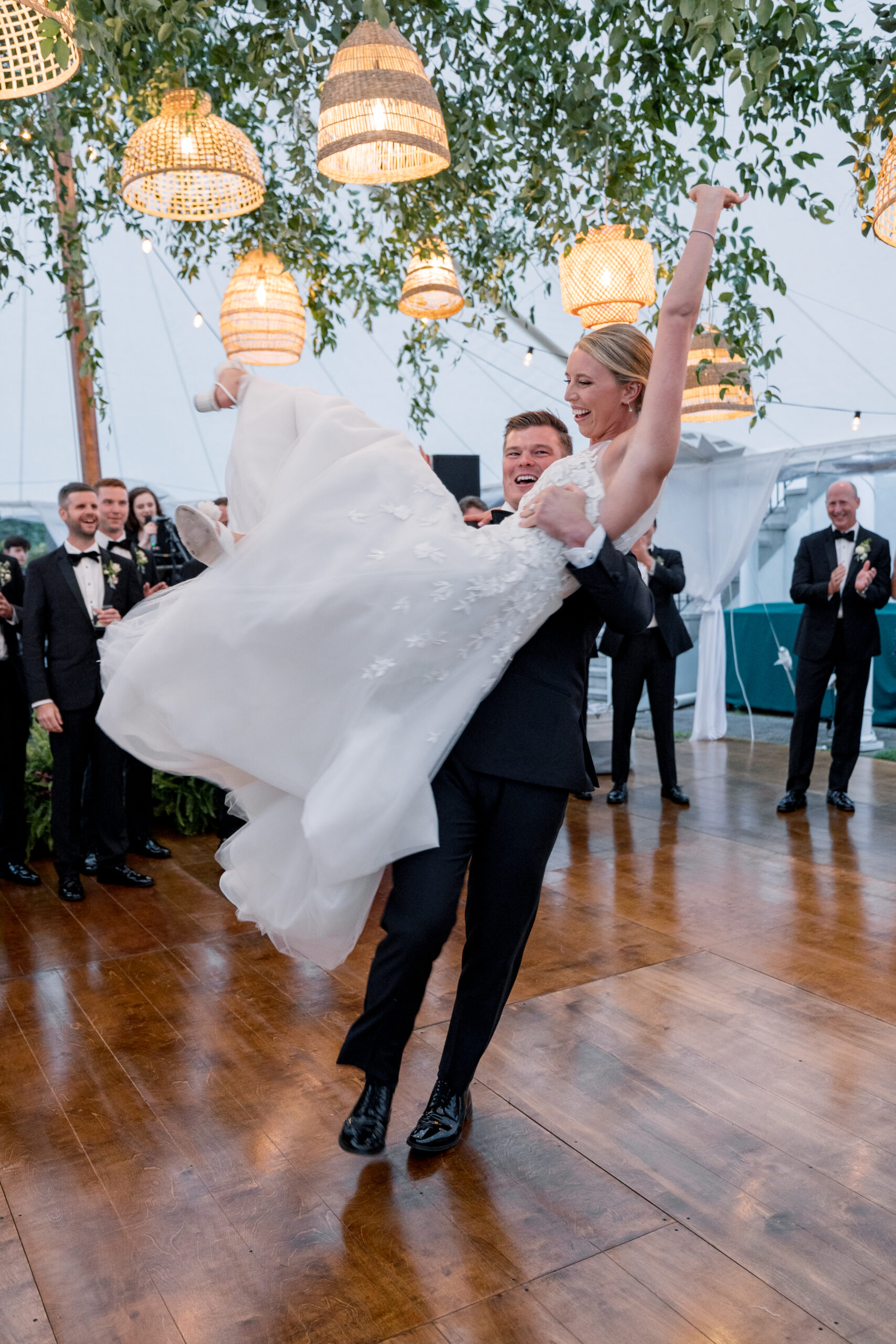 Groom lifts bride during a joyful first dance under woven pendant lights and greenery inside a tented wedding at Bald Peak Colony Club in New Hampshire.bald peak colony club wedding, new hampshire tented wedding, lake winnipesaukee wedding photographer, luxury wedding photographer new england, editorial wedding photography nh, first dance tented reception, romantic wedding moment new hampshire, destination wedding bald peak