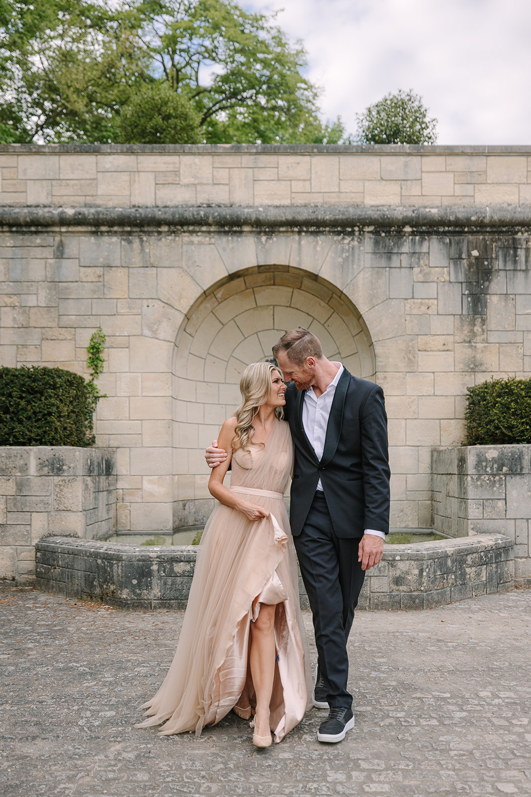 Couple Walk Through Historic Grounds of Parisian Chateau During Engagement Photoshoot