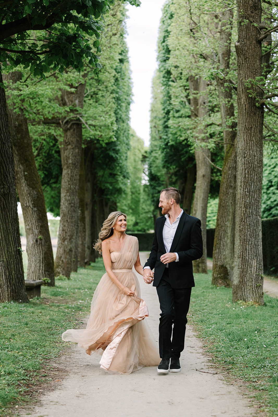Couple Holding Hands, Laughing, Running Through Gardens of Château de Sceaux During Spring, alley of trees in paris park