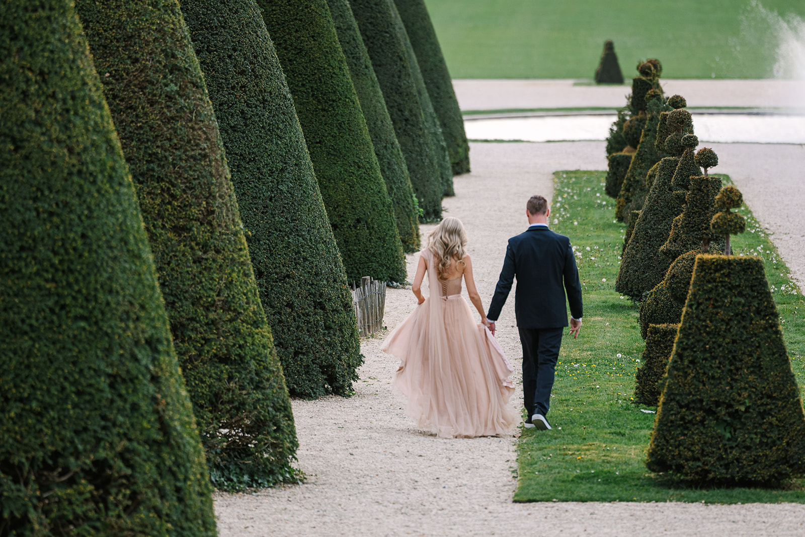 Photo of Engaged Couple From Behind Walking Through Gardens in Paris