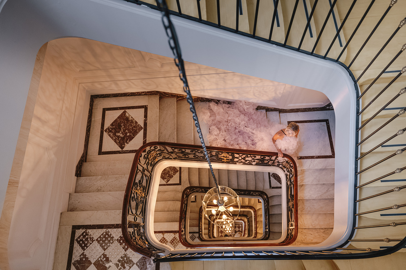 Overhead Photo of Woman Wearing Dramatic Layered Pink Tulle Dress with Long Train while Walking Down Winding Stairway