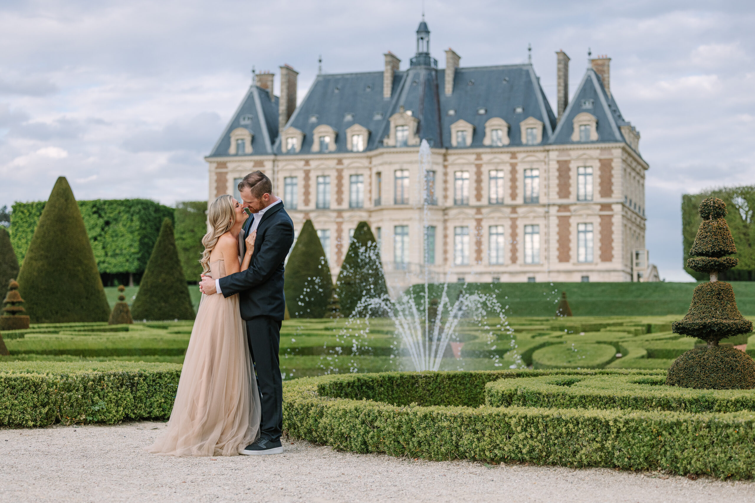 Engaged Couple Embrace in Gardens of Château de Sceaux, with Facade of Chateau in Backdrop, paris engagement session